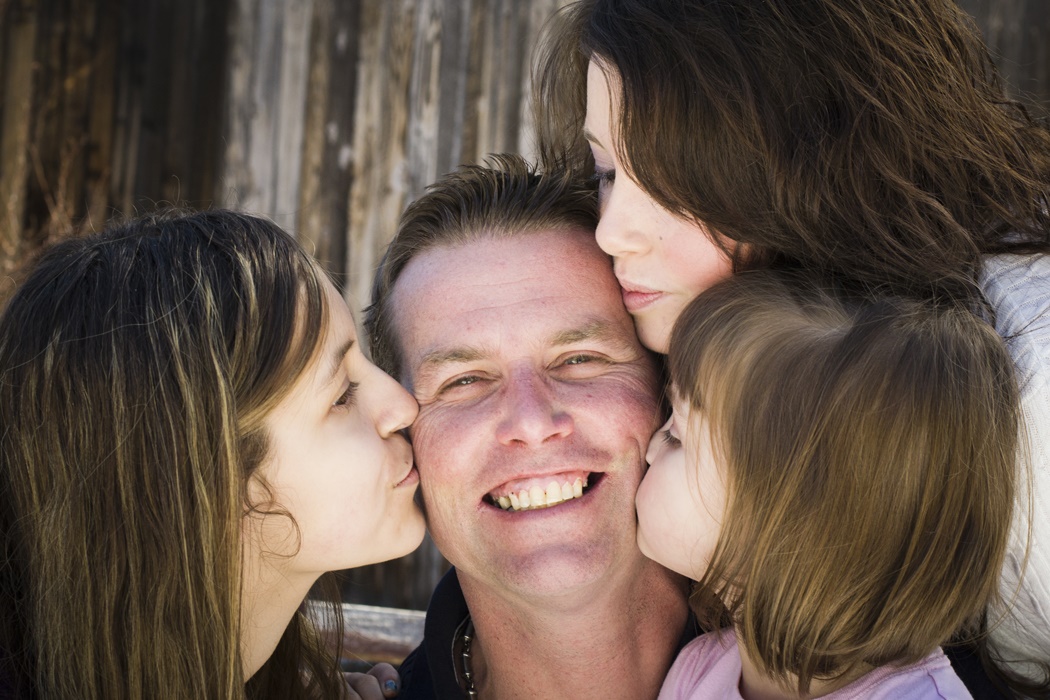Dad getting kissed by his daughters and wife.